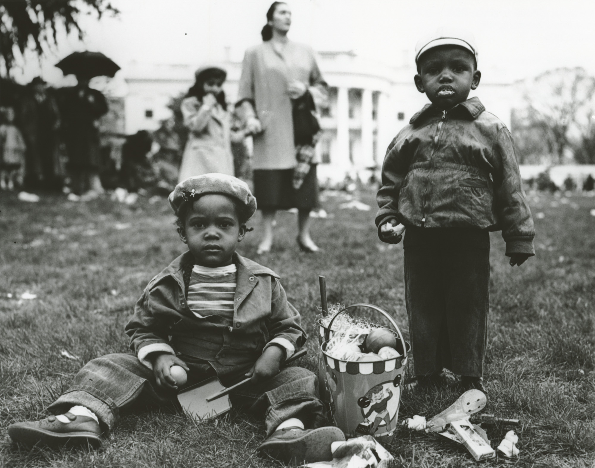 In this photograph taken by National Park Service Photographer Abbie Rowe on April 6, 1953, two young children enjoy treats from the their Easter basket at the annual White House Easter Egg Roll. (1953) (National Archives)