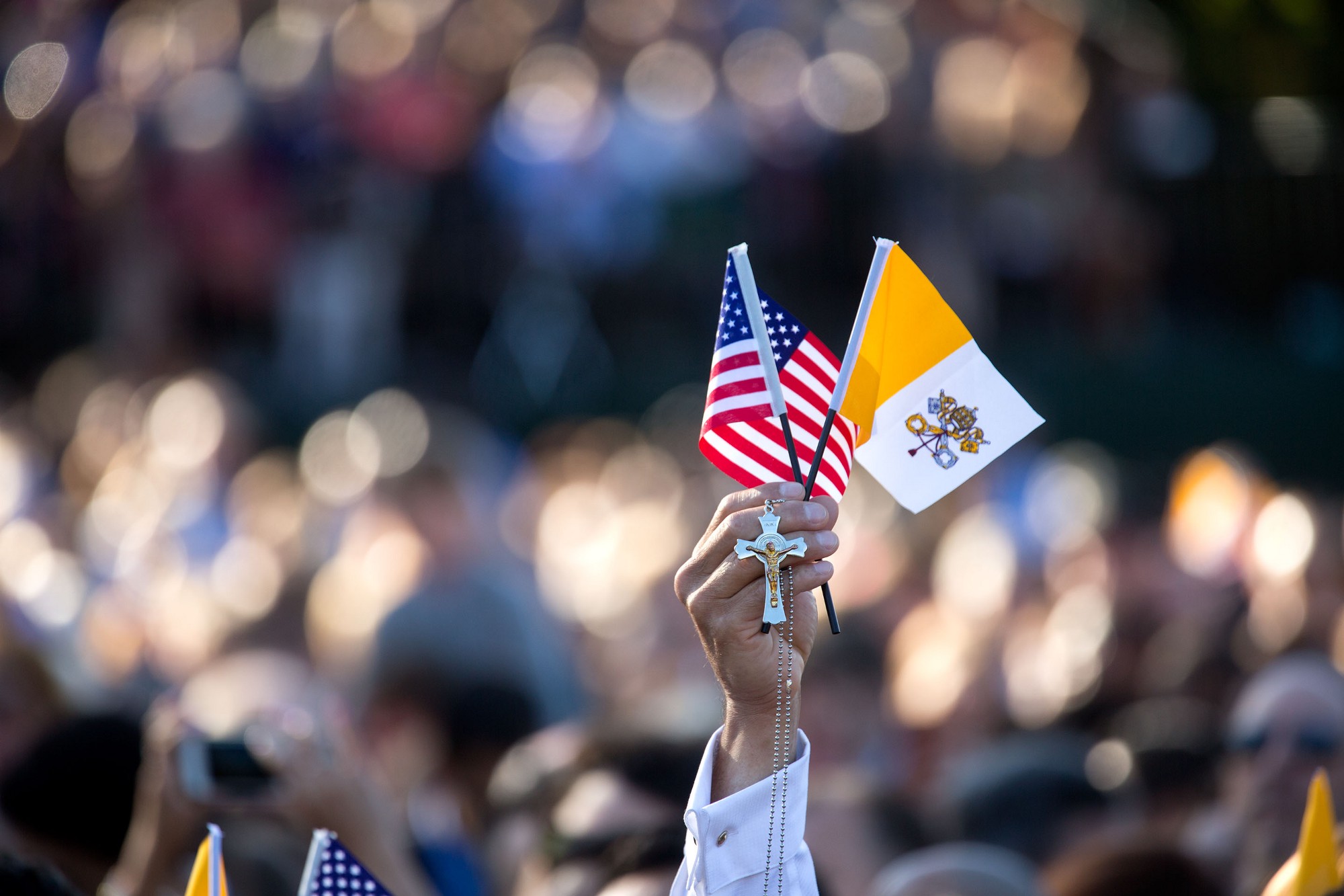 A guest holds up the American flag, the Vatican City flag, and a cross. (Official White House Photo by Lawrence Jackson)